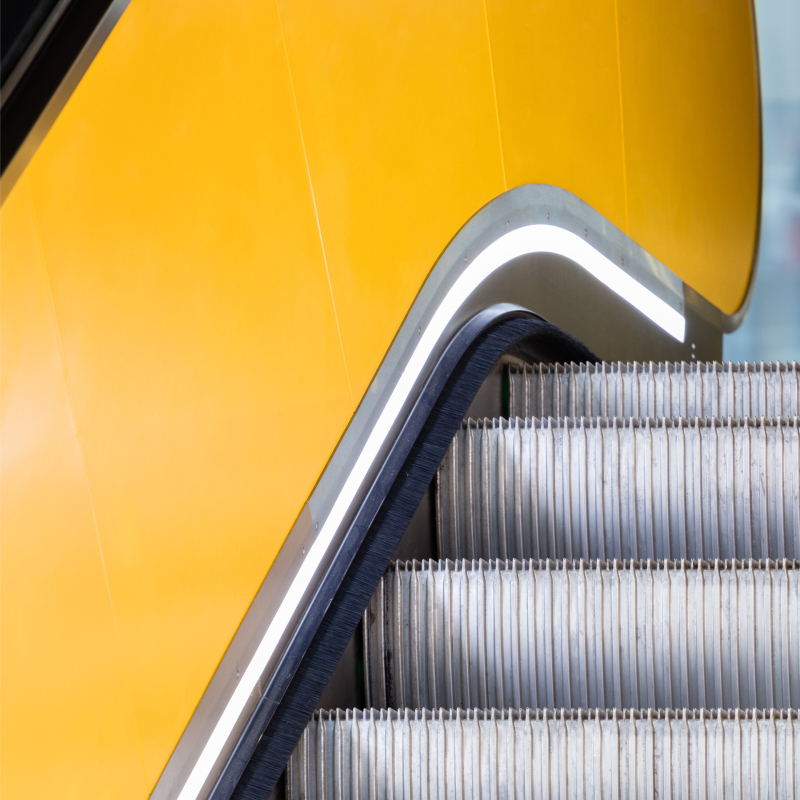 یک پله برقی زرد با نرده فلزی و دیوار زرد وجود دارد